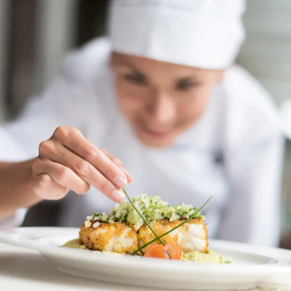 Chef concentrada en el emplatado de un plato gourmet, enfatizando la excelencia culinaria y la atención al detalle.