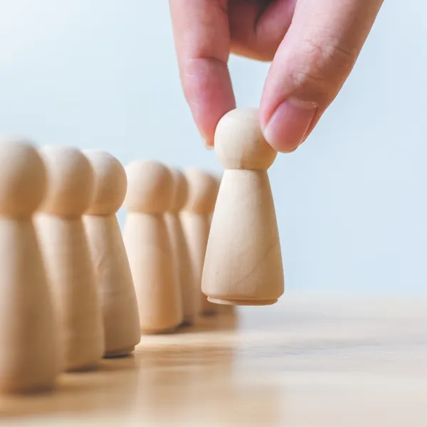 Mano seleccionando una figura de madera de entre un grupo similar, sobre fondo neutro.